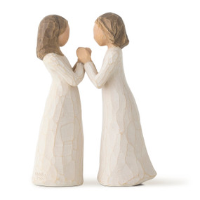 Front view of two standing female figures in cream dresses, facing towards each other holding hands