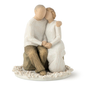 Front view of male and female couple figures sitting next to each other, holding hands on flat round base with carved white flowers