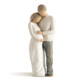 Front view of embracing male and pregnant female couple figures, female in cream dress, male in cream shirt and blue jeans