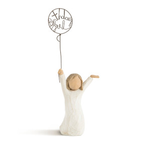 Front view of standing child figure in cream dress, holding wire balloon with words birthday girl" written in wire inside of it"
