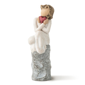 Front view of female figure in cream dress holding red heart sitting on gray rock etched with words and symbols of love