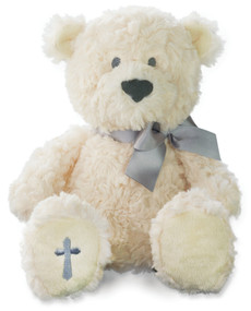 Cream stuffed teddy bear sitting up with grey bow and grey cross on bottom of foot