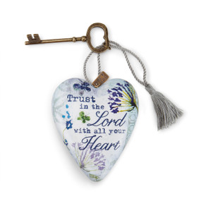 A white heart shaped sculpture with blue flowers that says "Trust in the Lord with all your Heart", with a silver tassel and metal key attached.