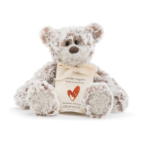 Light grey stuffed teddy bear sitting up holding tan keepsake bag that says 'loveable, huggable. always in my heart' above red heart