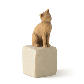 Figure of orange cat with tilted head perched atop a cream colored rectangular pedestal, facing right