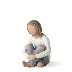 Front view of seated figure with long hair in cream shirt and blue jeans with arms wrapped around knees