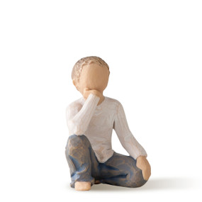 Front view of seated boy in cream shirt and blue jeans, resting arm on raised knee with hand under chin