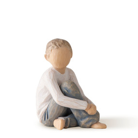Front view of seated boy in cream shirt and blue jeans, with arms around raised knees