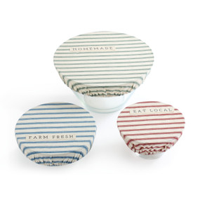 Three bowls laid out with covers on them - one is green stripe print with homemade on it, one is blue stripe print with farm fresh on it, one is red stripe print with eat local on it