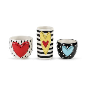 Set of three round mugs side by side - each is white/black polka dots and has different color heart in the center