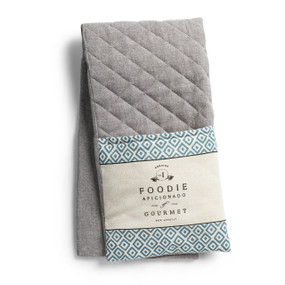 A grey double oven mitt with cream fabric ends that say "Foodie Aficionado of Gourmet" with a geometric border, displayed folded in half.