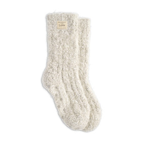 A pair of cream colored fuzzy socks with a small cream Giving Collection fabric tag attached.