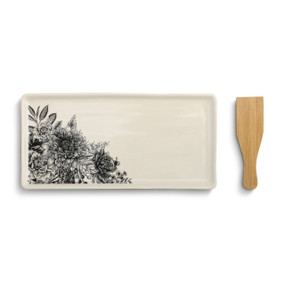 A white appetizer tray with black flowers. Placed beside a wooden spatula.