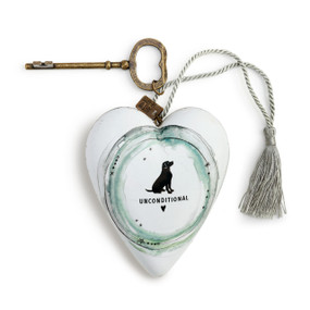 A white art heart with a dog drawing in the center, a bronze key, and a gray tassel.