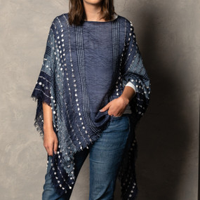 A close up image of a woman wearing dark denim jeans, a white shirt, and a textured navy poncho.