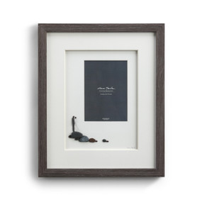 A dark gray picture frame enclosing a pebble scene of a newly wed couple.