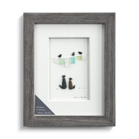 A gray frame enclosing a pebble scene of two kittens looking at birds on a clothesline.