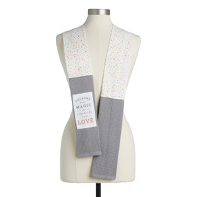 A white polka dot fabric kitchen boa with gray towel ends and a white fabric patch that says "Grandma Bakes Magic and Sprinkles it with Love" displayed on a mannequin.