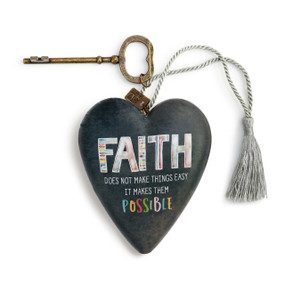 A black art heart that reads "faith does not make things easy it makes them possible", with a bronze key and a gray tassel.