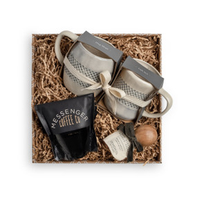 A brown gift box filled with a bag of Messenger Coffee, a mini wooden scoop, and a pair of coffee mugs.