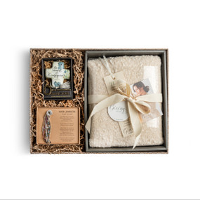 A brown gift box filled with a cream "Giving Shawl", a beige art cross, and a "Your Journey" bracelet set.
