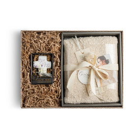 A brown gift box filled with a cream "Giving Shawl" and a beige art cross.
