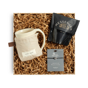 A brown gift box filled with a bag of Messenger Coffee, a black cord bracelet with a silver pendant with a paw print, and an ivory coffee mug in a sleeve that reads "cat mom".