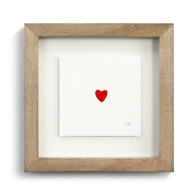 A white piece of paper with a red thread heart in the center placed in a wooden frame.