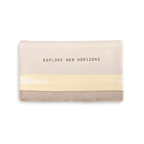 A beige and ivory spoon rest with a yellow plain and "explore new horizons" engraved.
