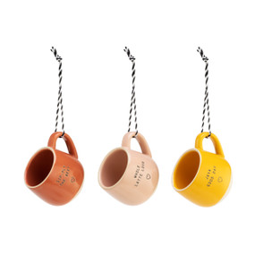 A set of three small coffee pod mug ornaments. One red and reads "sip-ply the best". One light pink and reads "whole latte love". One yellow and reads "java good day". Each with a black and white striped string.