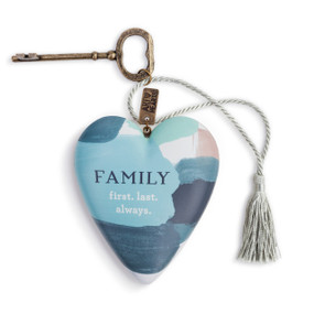 An art heart with several colored paint strokes, such as pink and blue, and reads family first. last. always." in the center. With a bronze key and a silver tassel."