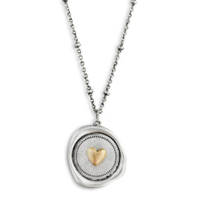 A close up image of a circular pendant with a gold heart and a circular polka dotted border  on a dainty silver necklace.