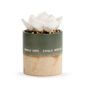 A small, speckle textured, tan and dark teal vase that reads inhale hope, exhale worries", filled with an assortment of small rocks, and a white succulent oil diffuser."