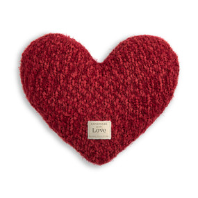 A red heart shaped Giving Collection pillow with a small cream Giving Collection fabric tag attached.