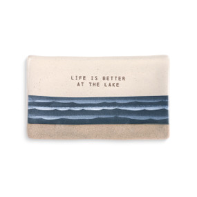 A beige and ivory spoon rest with blue waves and "life is better at the lake" engraved.