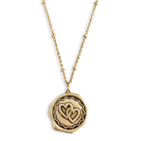 A close up image of a circular pendant with two interlocked hearts on a dainty gold necklace.