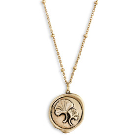 A close up image of a circular pendant with two flowers on a dainty gold necklace.