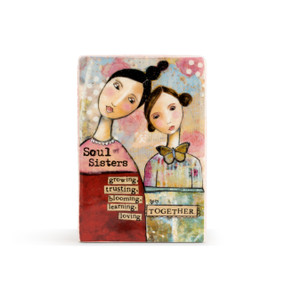 A cream rectangular plaque with a collage of patterns, two young sisters, and reads Soul Sisters growing, trusting, blooming, learning, loving together." in black typewriter font."