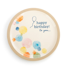 A circular white and tan ceramic plate with small multi color polka dots, a simple blue balloon drawing, and reads "happy birthday! to you..." in blue font.