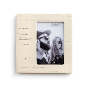 A textured cream colored picture frame, with thin brown stripes, reads My dearest, I love you. It is as simple, and wonderful, as that" in blue typewriter font, and is filled with a couple's photo."