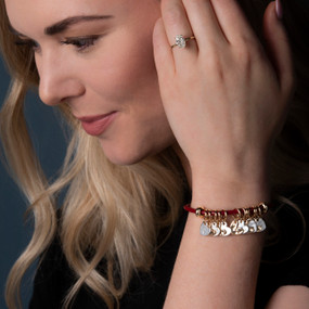 Close up of a woman wearing a red leather bracelet with multiple gold and silver heart charms.
