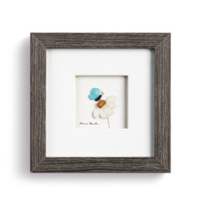 A pebble scene of a butterfly on a flower, enclosed in a dark wooden frame.