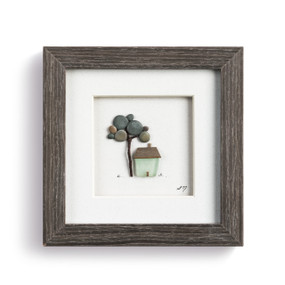 A pebble scene of a home and large tree, enclosed in a dark wooden frame.