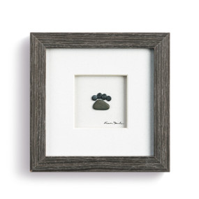 A small paw made from pebbles, enclosed in a dark wooden frame.