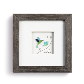 A pebble scene of a flower and hummingbird enclosed in a dark wooden frame.