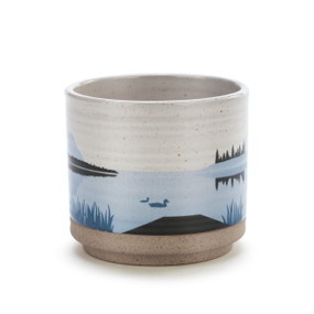 A round ceramic container with a lake scene including a dock, ducks and the water in shades of blue.