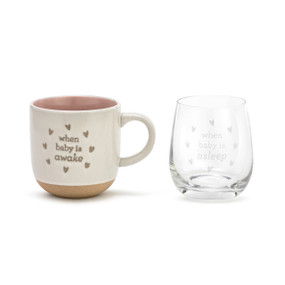 A front facing view of a cream ceramic coffee mug that reads "when baby is awake", placed beside a wine glass that reads "when baby is asleep".