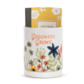 A white ceramic planter that says "Goodness Grows" and has a yellow paper journal inside that says "seeds of thought".