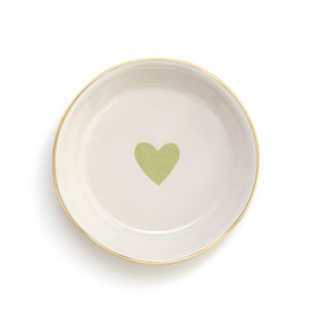 An overhead view of a small white ceramic dish with a light green heart and a gold rim.