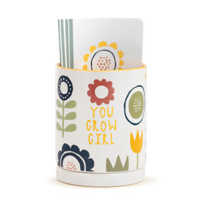 A white ceramic planter that says "You Grow Girl" decorated with simple bold flowers and has a paper journal inside.